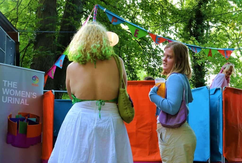 Two festival-goers queueing for a Peequal urinal.